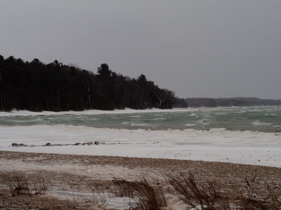 Landscape image of a white capped Lake Michigan, with sand and a snowy shoreline.