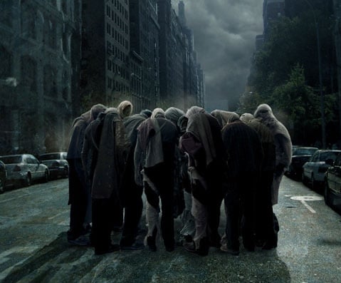 A huddled group of shadowy figures stands with heads bowed in the middle of a city street.