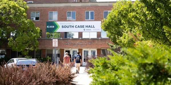 Exterior photo of South Case Hall, with two students walking into the building with their backs to the camera.