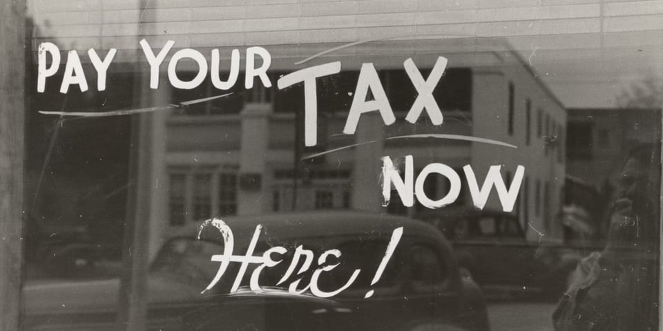 A black and white window display that says Pay Your TAX Now Here!