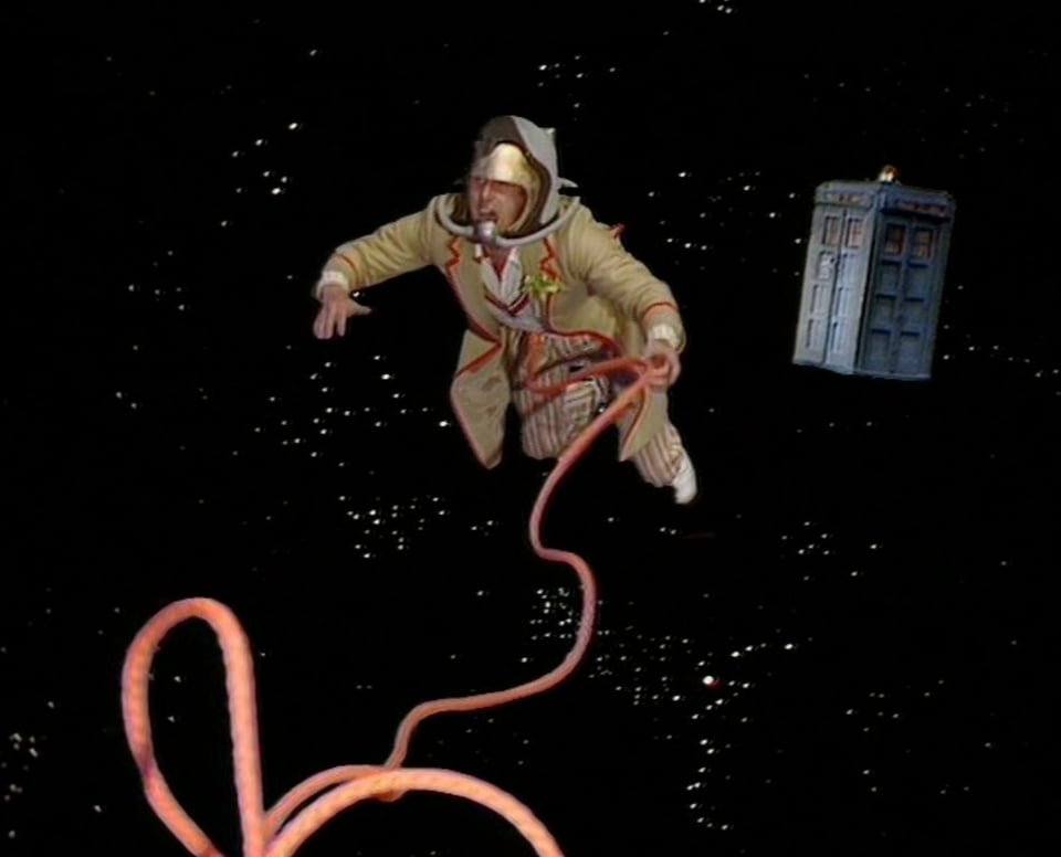The Fifth Doctor floats in space attached to a tether, with a police box behind him. He has just thrown a cricket ball.