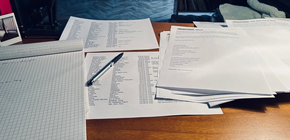 photo from writing desk, with sheaves of printouts, a notebook & pen, an Instax of an empty chair, and other signs of the author/photographer's genius