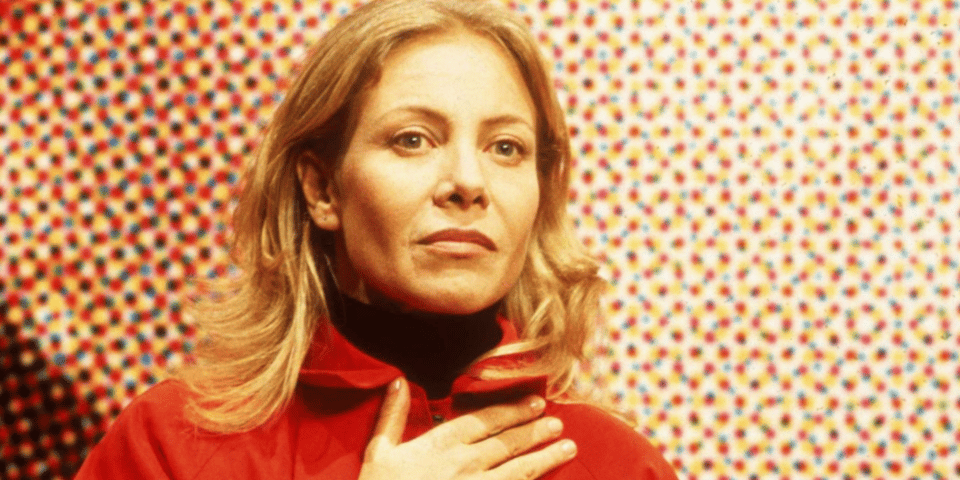 A woman in red standing in front of a colorful pixelated background.