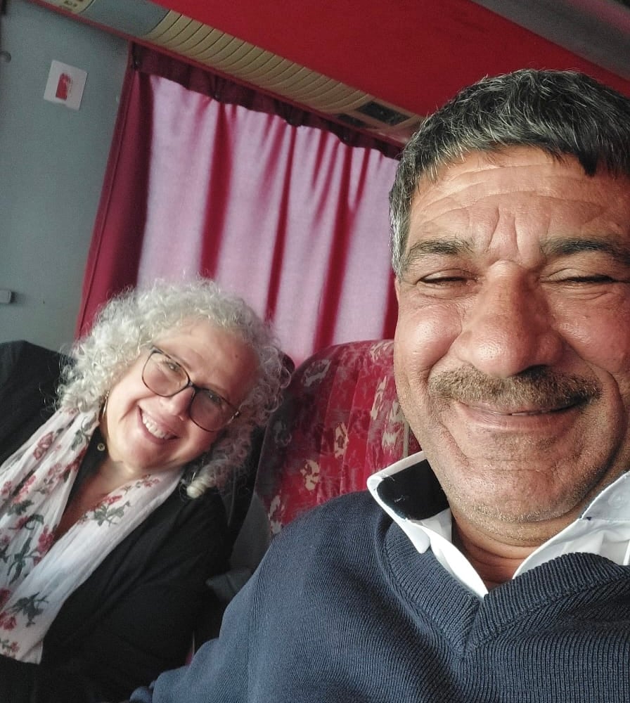 Two smiling people sitting in the front row of a bus 