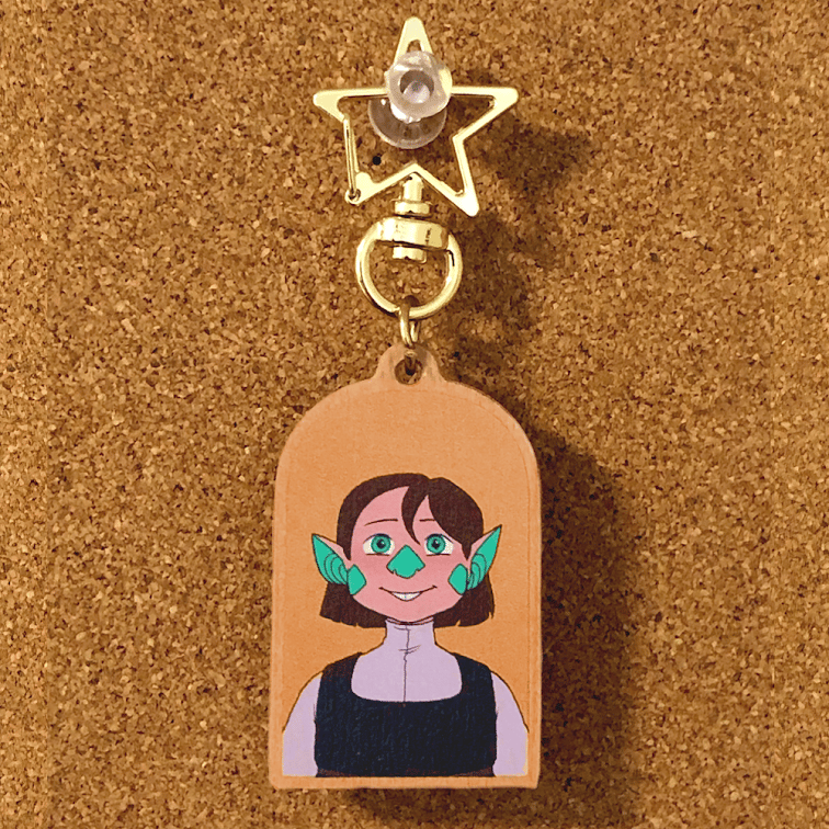 A photo of Ellie from Runaway Drakaina on an arch shaped wooden keychain with a star shaped clasp.