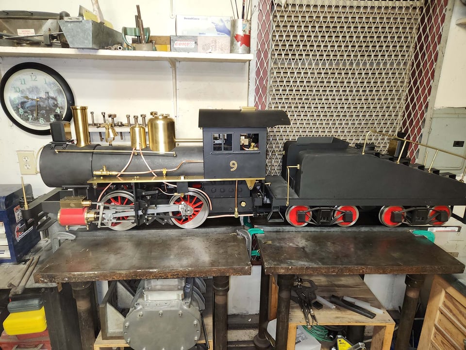 A black model steam engine with red wheels and brass accents.