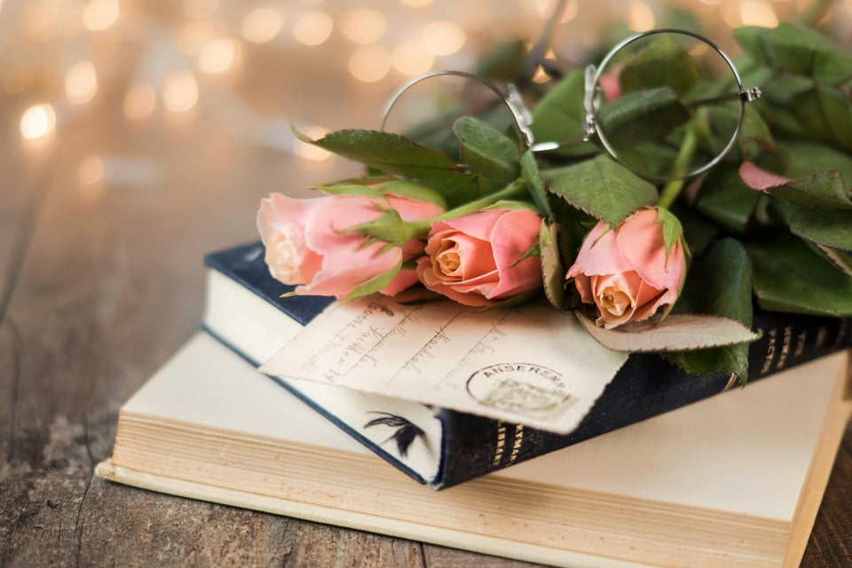 Stock image of flowers and apostcard piled on top of two books.