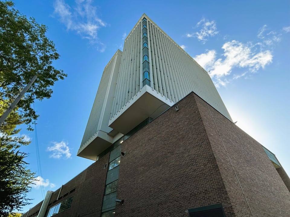 A six storey tower block hovering over a brick block. From this angle, the pediment it rests on is just visible.