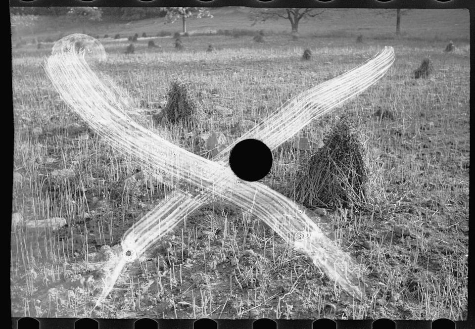 An black&white image of a field with several small haystacks. There is a white x across the image done with with looks like a brush. There is also a black hole in the circle, where a hole punch has been used.