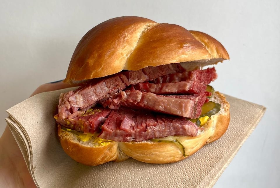 Our Salt Beef sandwhich, a bun containing red beef on pickles and mustard.