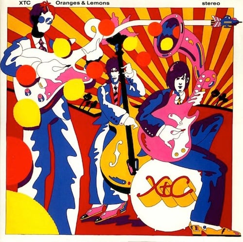 A cartoonish drawing of the member of XTC done in a psychedelic, YELLOW SUBMARINE (the movie) way. It's full of color, lots of reds, yellows, oranges and deep blues. One figure is playing a guitar, and the neck of the guitar is turning into the airstream of a jet fighter airplane. Another guitarist sits on a bass drum labled XTC. Behind them is a guy playing standup bass. There is a pink horn shooting out oranges and lemons behind them.