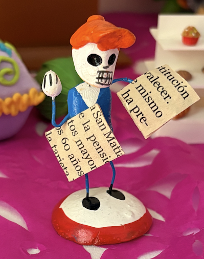 A Day of the Dead style skeleton figurine holding miniature newspapers.