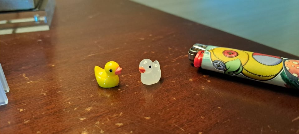 Two tiny rubber ducks next to a cigarette lighter