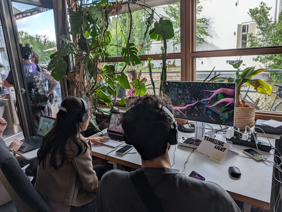 Two people play a videogame in front a lush, verdant windowscape.