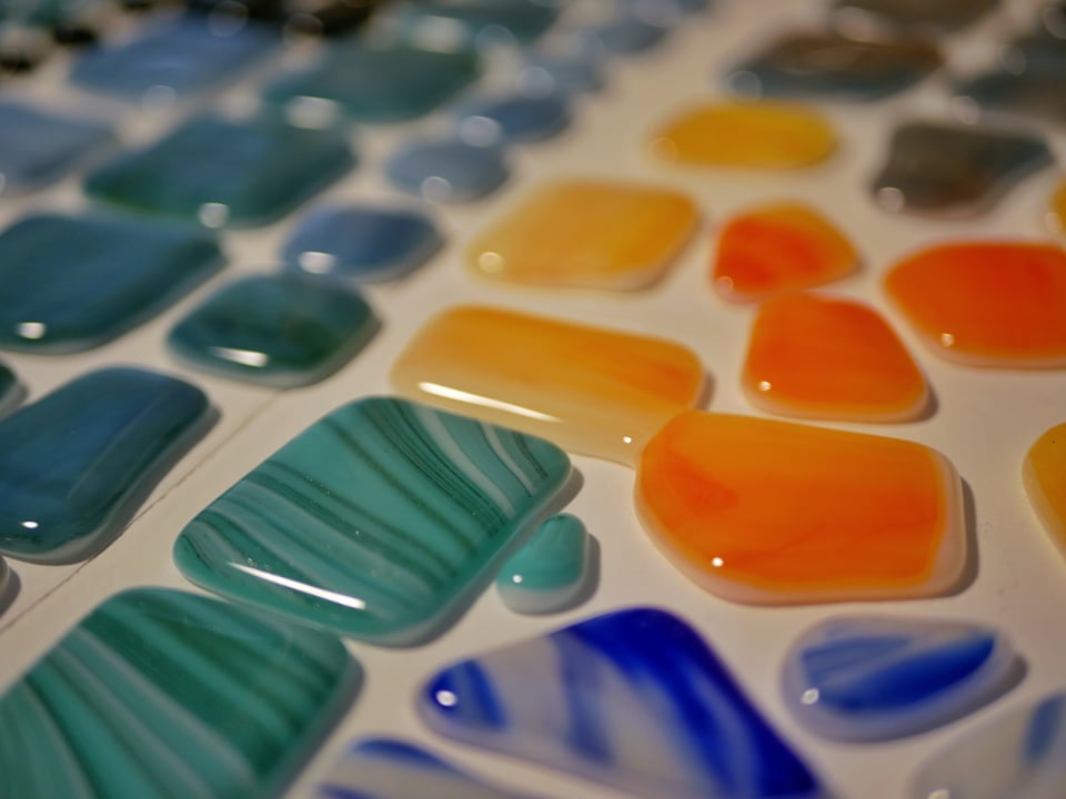 kiln shelf with a bunch of cabochons on it from a slight angle. teal and yellow/orange are visible