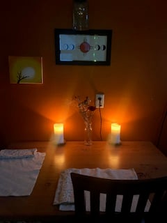 glowing pillar candles on the kitchen table in darkness, in front of an orange wall with solar-themed art