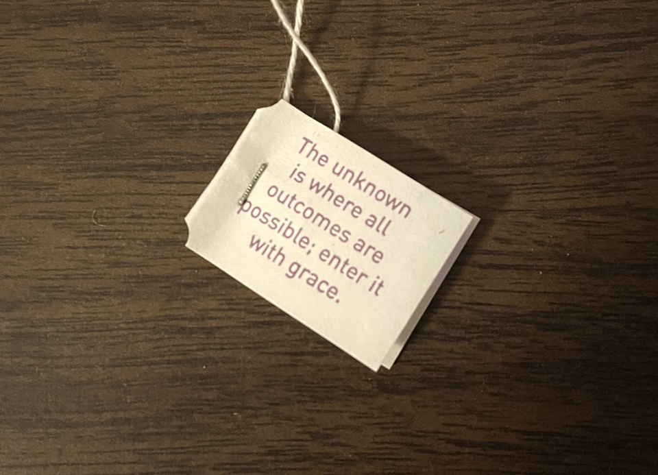 A tab on the end of a tea bag with the words "The unknown is where all outcomes are possible"