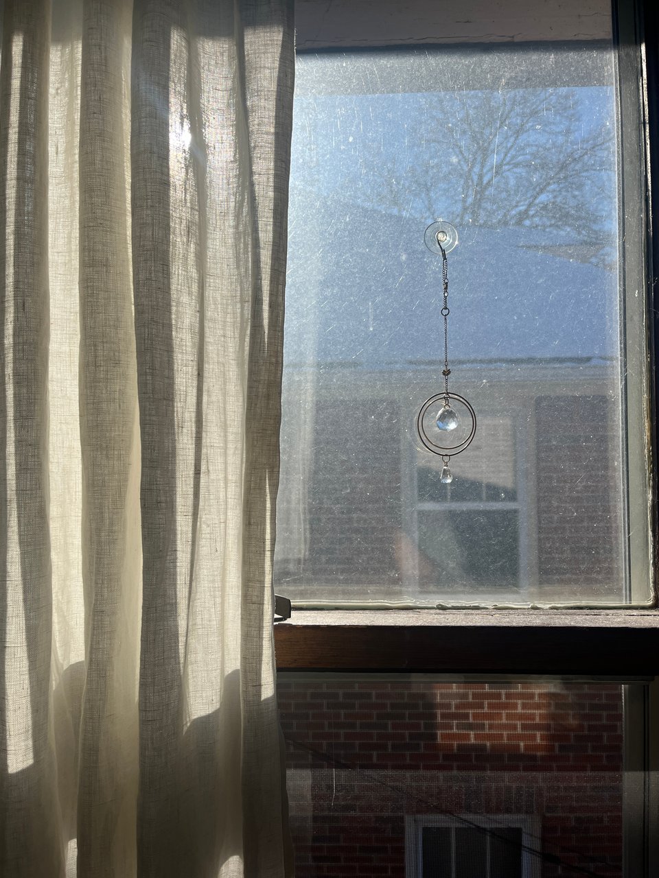 sunlight through a half-curtained window with a hanging double prism