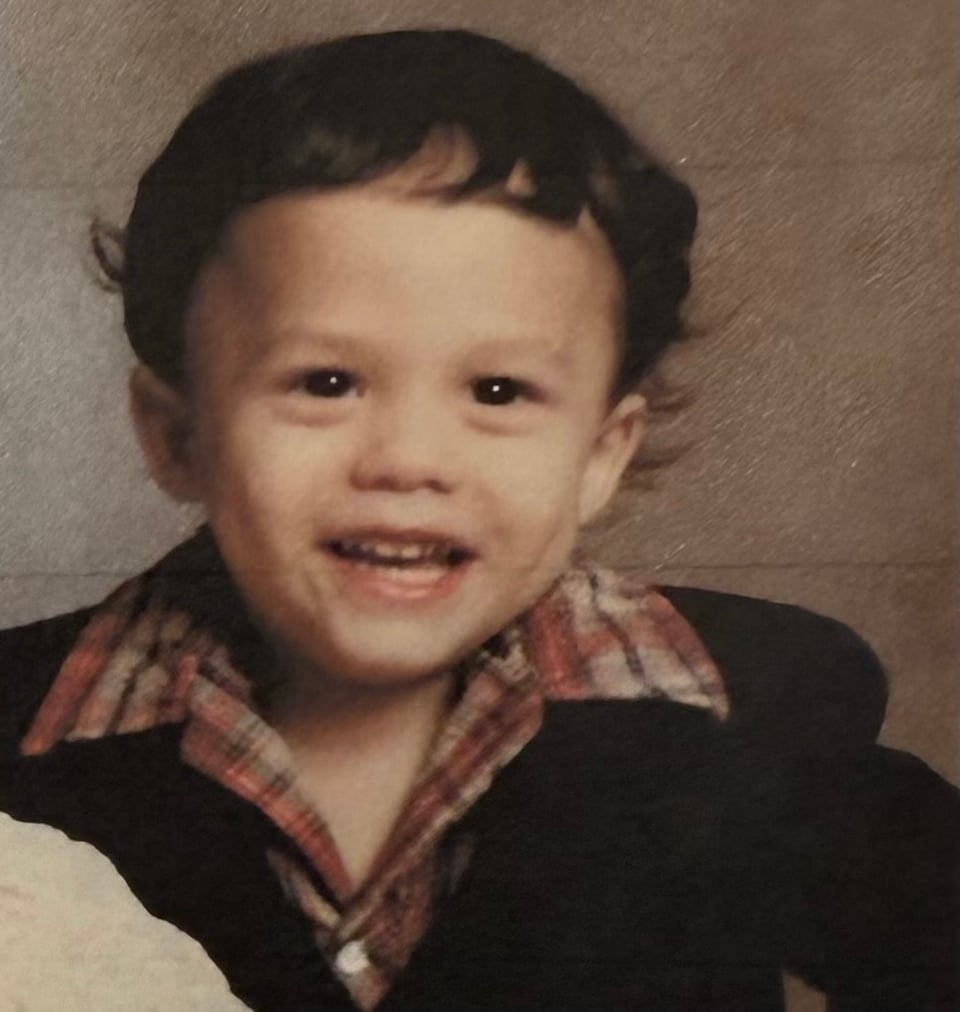 the author when he was a toddler, wearing an open-collar button down shirt under a blazer, smiling with his mouth open in a cropped family photo