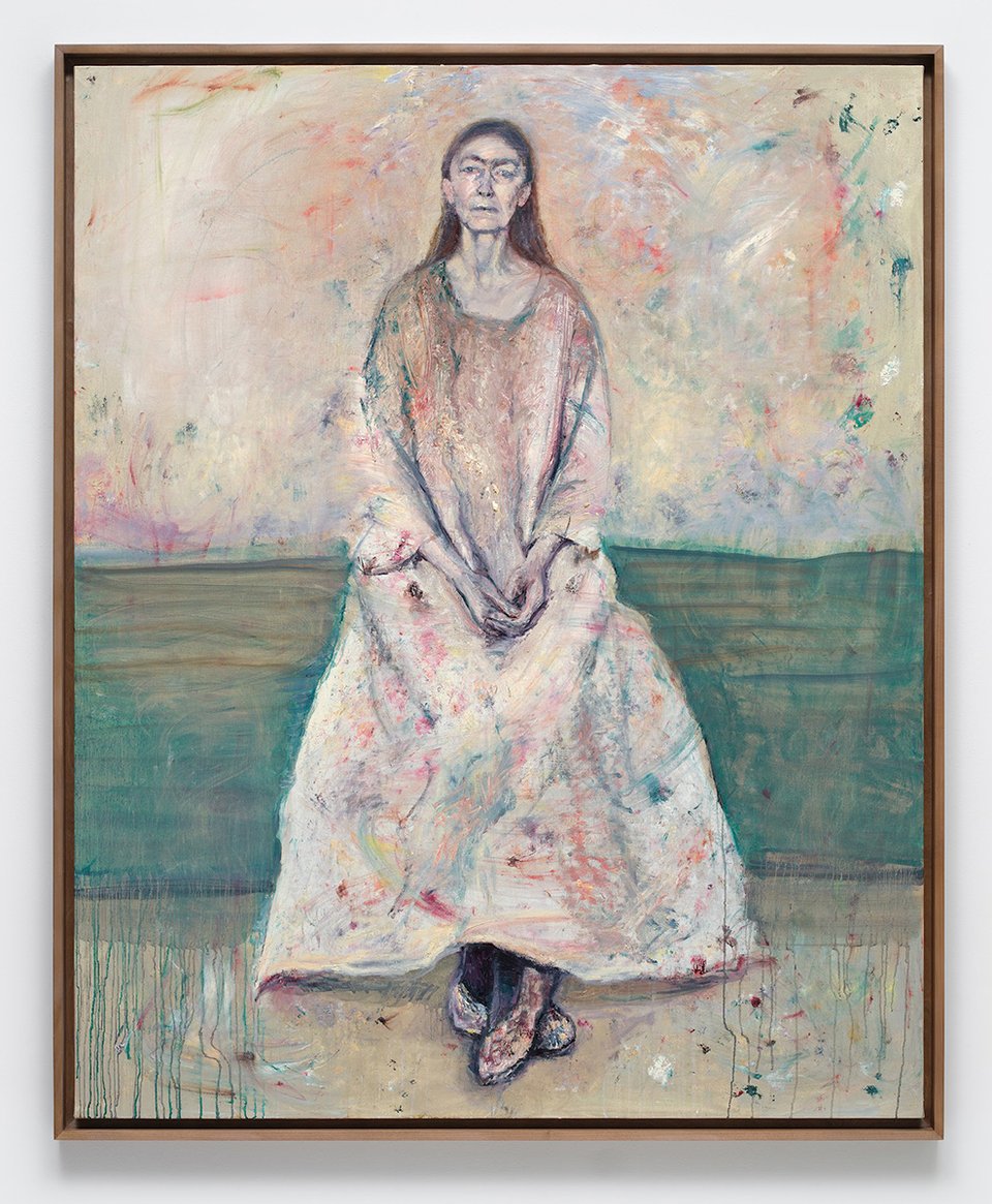 Photo of a painting of the artist Celia Paul, seated. She's in a pale frock that is covered with paint, and the wall/background is a similar set of colors.