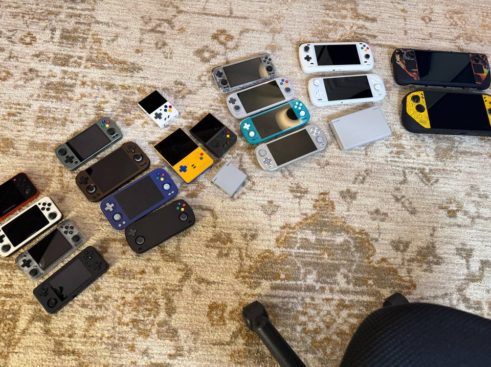 21 retro gaming handhelds arranged on a beige rug