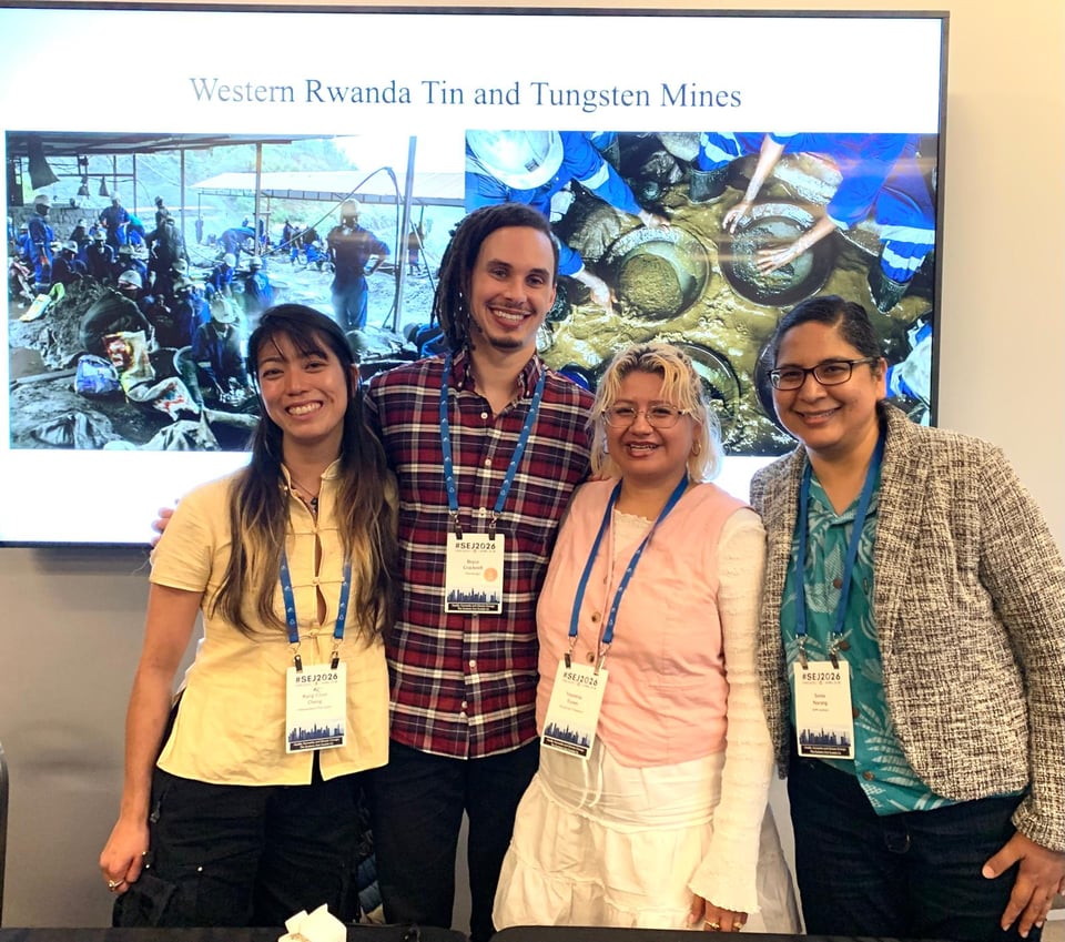 Four journalists pose in front of a slide deck showing photos from western Rwanda tin and tungsten mines