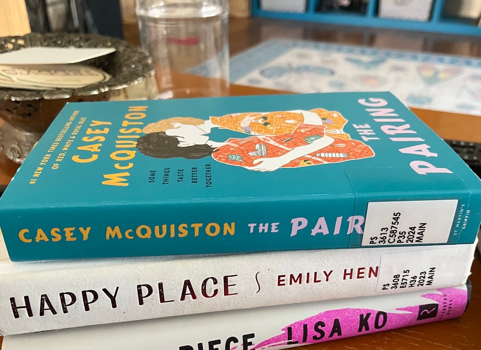 A stack of books on a coffee table with a candy jar and knick knacks in the background.