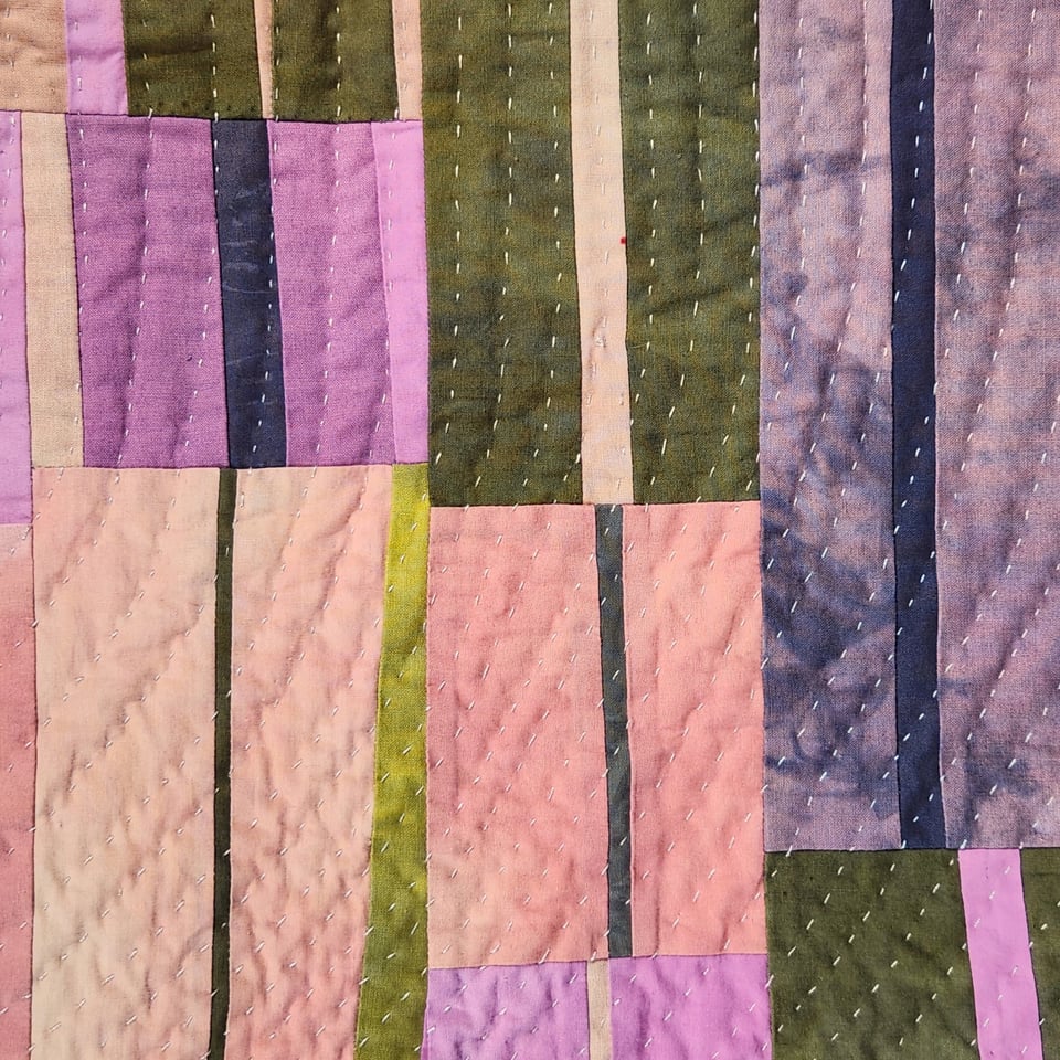 Detail view of Sarah Atlee’s patchwork quilt titled Arabesque I. The quilt is made from hand-dyed fabrics in pink, orange, grey, purple, and yellow green.