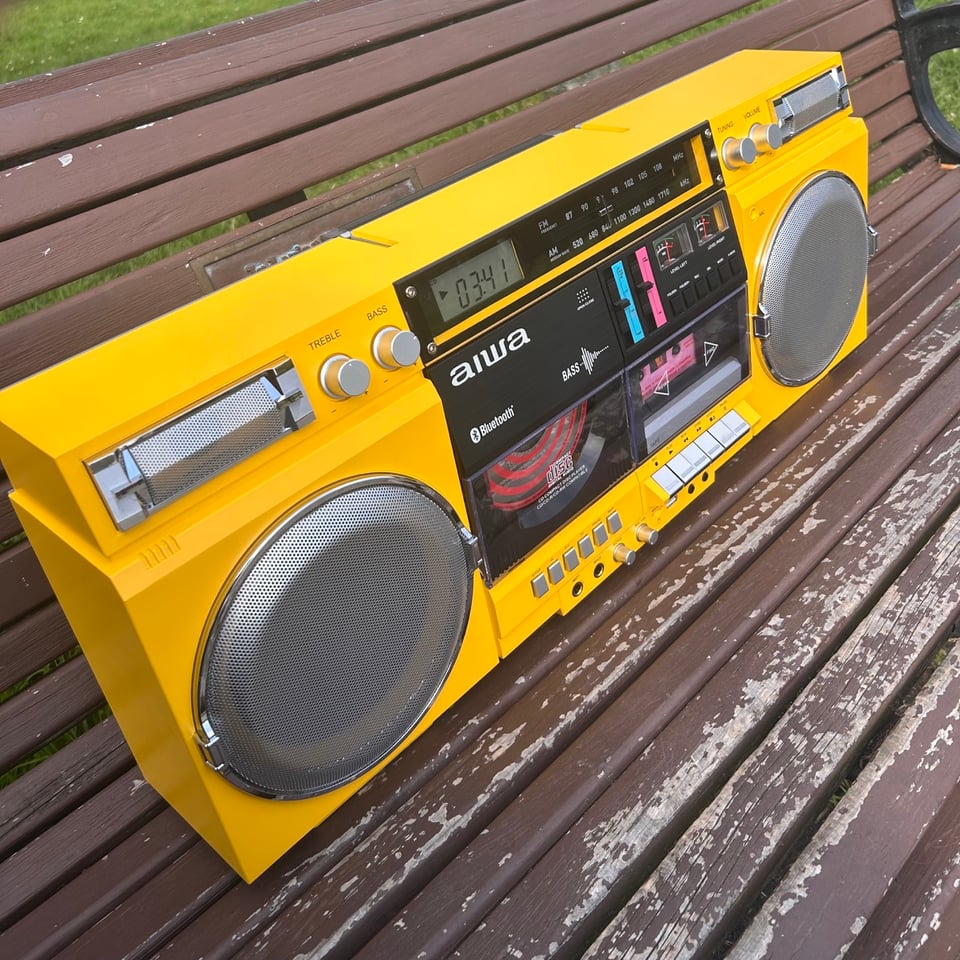 A ridiculously large yellow boombox sitting on a park bench.