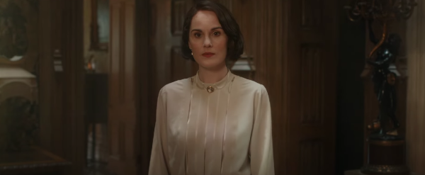 Michelle Dockery, as Lady Mary, is wearing a white blouse and standing in the hall of 'Downton Abbey'.