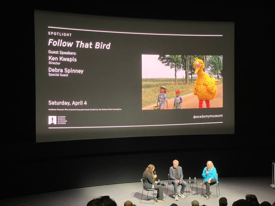 A large screen advertises the film Follow That Bird. Beneath it, three people sit in conversation during a Q&A