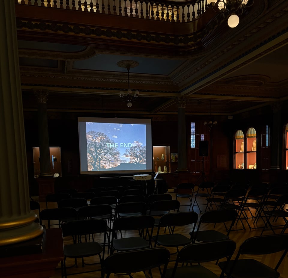 Empty seats in screening area of the ballroom, with a projector screen showing the end of Oaks, with text that reads "The End" and silhouetted oak trees.