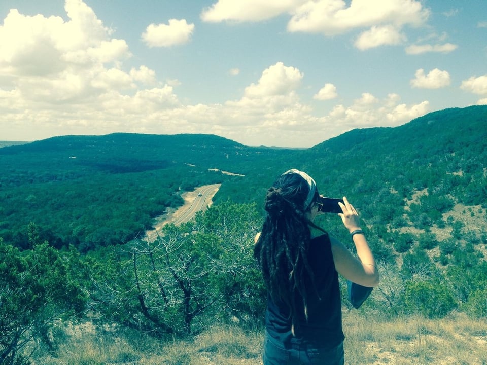 Photo of Destiny from behind, taking a picture of a mountain landscape while on a hike