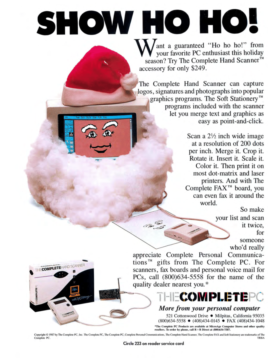 A computer monitor with a Santa hat atop it and a fake white beard in front of it. There is a device attached to the monitor and sitting on top of a drawing of a face, the same drawing appears on the computer monitor.