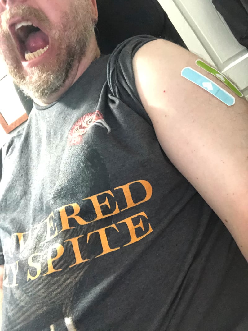 An old white man wearing a t-shirt with a turkey vulture on it, with caption "Powered By Spite". The man roars Hulk-like with all the power from multiple vaccinations.