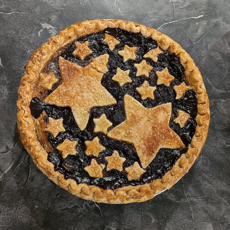 a photo of a berry pie with crispy golden stars, some big and some little, sprinkled across the top in lieu of a more traditional lattice crust.
