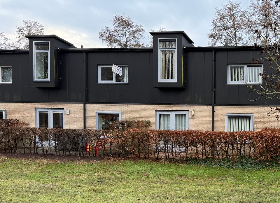 The back side of a row of houses with a "te koop" (for sale) sign stuck to one window.