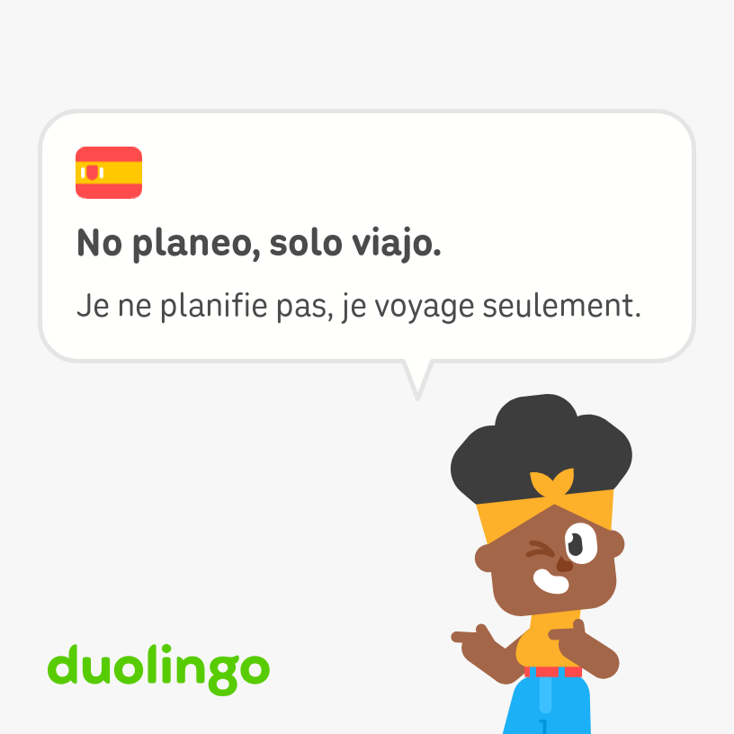 A cartoon of Bea, Afro-Latina foodie of Duolingo, with a speech bubble that reads, “I don’t plan, I only travel,” in Spanish and French. Bea wears jeans with a red belt, and a yellow sleeveless top with matching scarf around her hair. She's winking and pointing with her trademark finger-guns at a light green "duolingo" logo