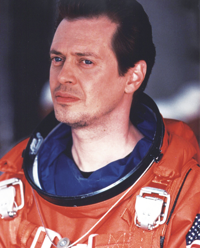 The actor Steve Buscemi in an orange space suit with no helmet, looking pensive