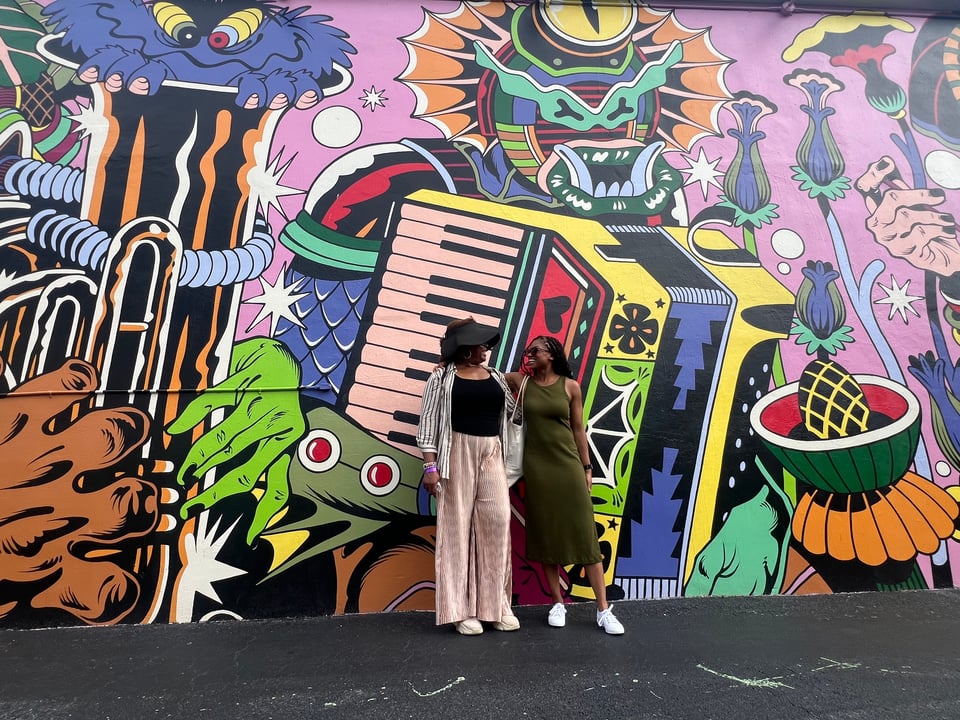 Me and my mother in front of a colorful street muralm featuring abstract and cartoonish designs, including a frog and various fantastical creatures.