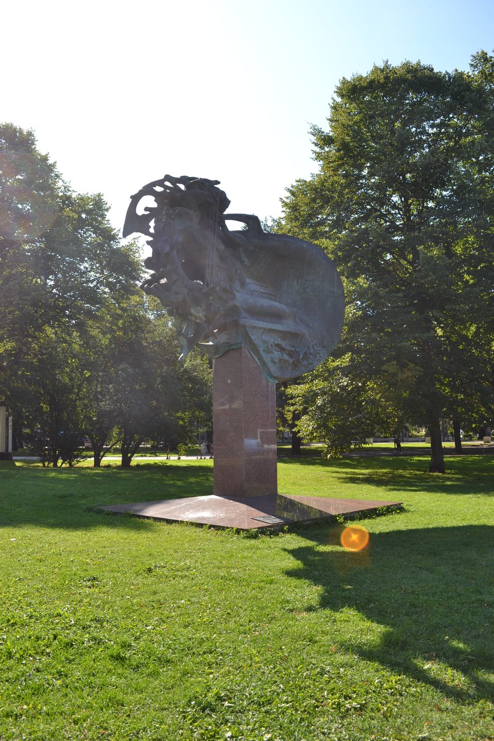 A sculpture of a highly stylized ear set in a wooded park.