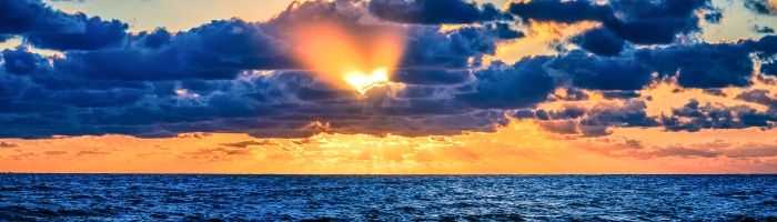 Blue clouds over the ocean with a heart-shaped gap through which sunlight is streaming