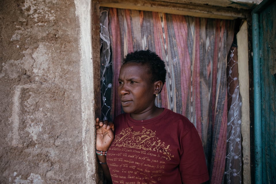 Lucy Kagure stands outside the door and looks away from the camera