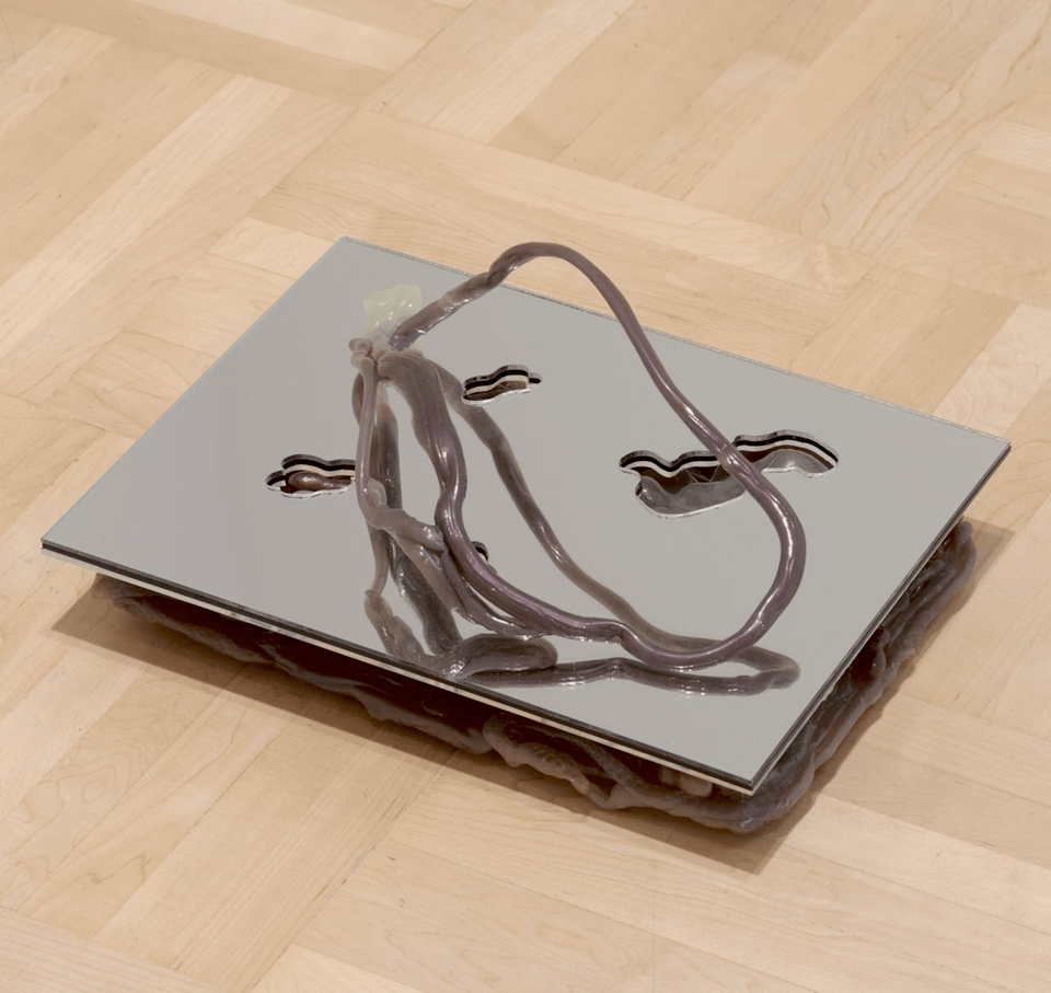 a flat mirrored sculpture with oddly shaped cutouts and a squiggly plastic arch