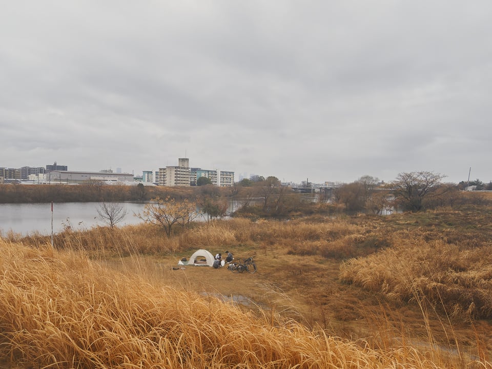 Boys camping along the Shonai River. Nagoya in the distance. Cloudy skies.