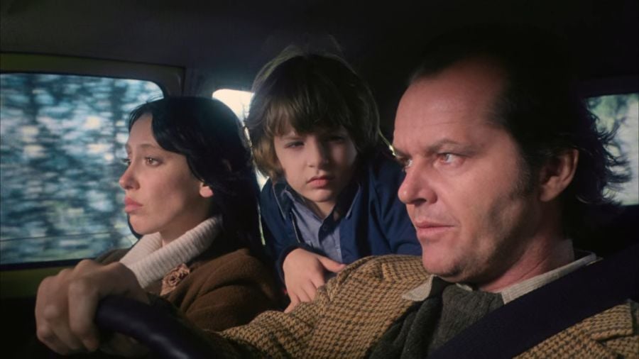 Shelly Duvall, Jack Nicholson, and Danny Lloyd. The two adults are sitting in the front of the car, Danny is in the back, but he is leaning forward to look at his father as they discuss cannibalism.