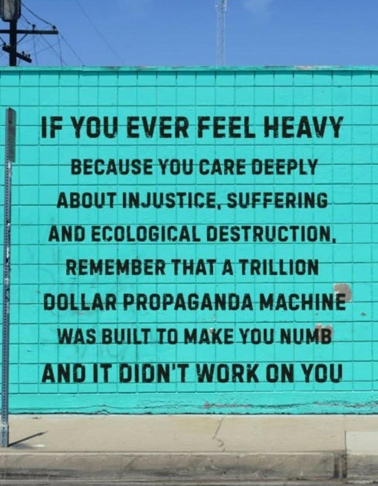 Sign reading "If you ever feel heavy because you care deeply about injustice, suffering and ecological destruction, remember that a trillion dollar propaganda machine was built to make you numb and it didn't work on you"