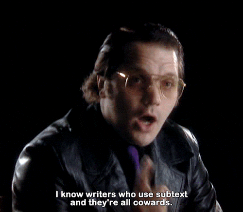 A very hip-looking author wearing tinted glasses and a black leather sport coat is commenting to an interviewer. The text transcription reads "I know writers who use subtext and they're all cowards."
