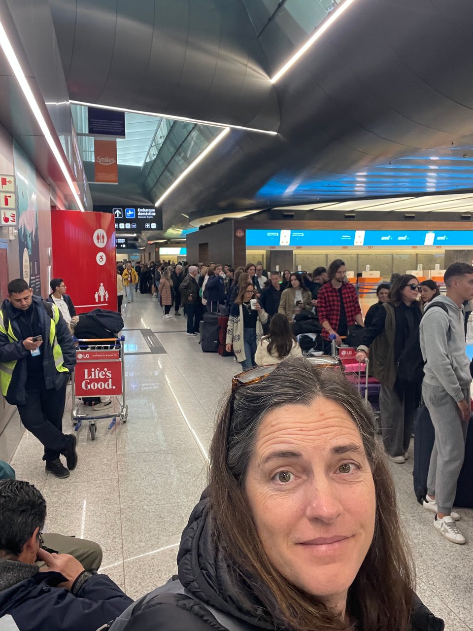 A woman looks up at the camera with a very long line of people at the airport next to and behind her.
