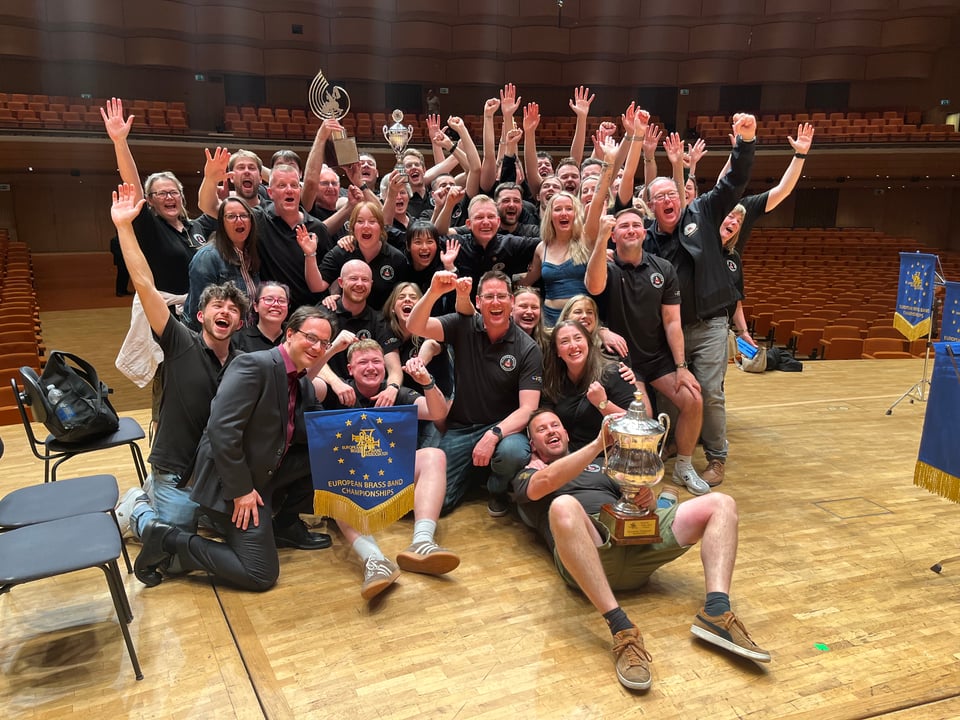 A group of extremely excited banders on stage, cheering and holding a variety of silverware.